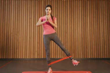 A woman performs leg exercises with a resistance band at a gym, promoting fitness and healthy living.